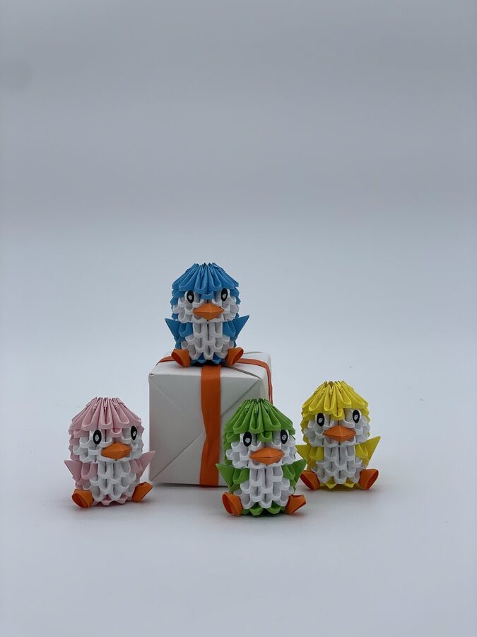 4 canards origami 3D colorés autour d'une boîte cadeau